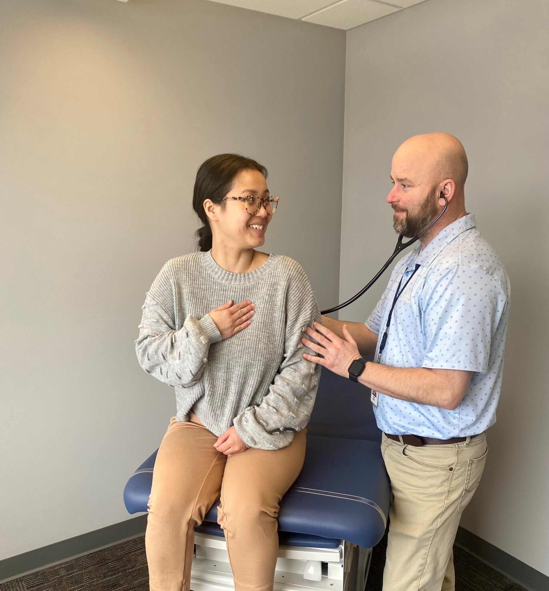 man with stethoscope talks with woman sitting on exam table